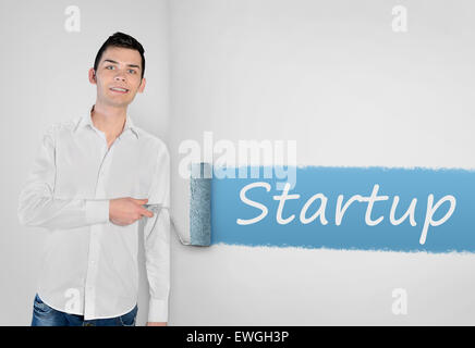 Young man painting Startup word on wall Stock Photo