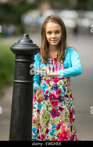 Little cute girl washes hands under water hand pump on the street in the old town. Stock Photo