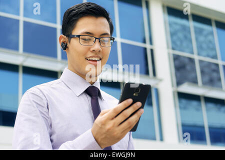 Young chinese businessman doing video conference call on smartphone and talking with bluetooth headset device in the street Stock Photo