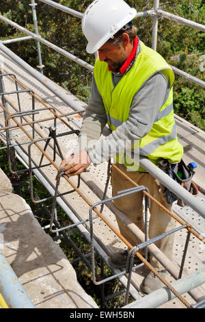 Worker setting steel reinforcing bars for reinforced concrete wall on historic stone road bridge Stock Photo