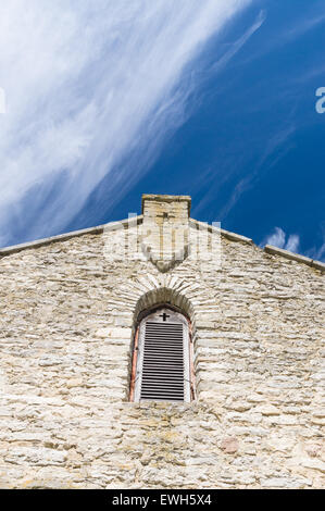 Limestone facade of ancient church with window shutter and cross shape in wall Stock Photo
