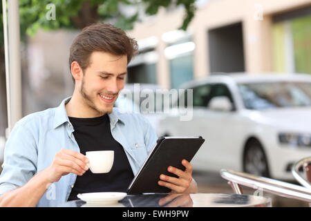 Happy man reading an ebook or tablet in a coffee shop terrace holding a cup of tea Stock Photo