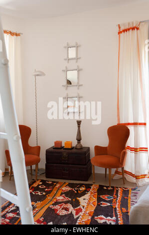 Pair of 19th century Italian chairs flank vintage trunks in room with Moroccan rug and white and red curtains made from saris Stock Photo