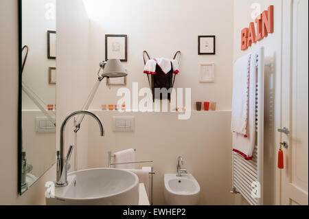 Bright modern bathroom with heated towel rail, colourful lettering and lamp by Artemide Stock Photo