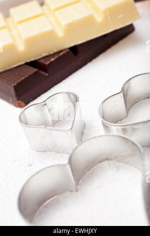 Cookie cutters and white and dark couverture chocolate on floured baking mat Stock Photo