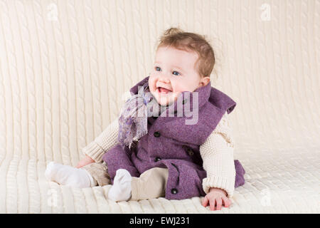 Cute laughing baby girl in a purple jacket sitting on a knitted blanket Stock Photo