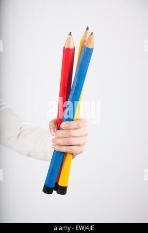 closeup of blue red and yellow primary colours big pencils in woman hand fingers isolated over white background Stock Photo