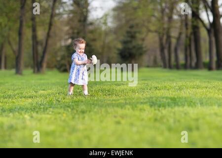 Beautiful baby girl in a blue dress running with a big white aster flower Stock Photo