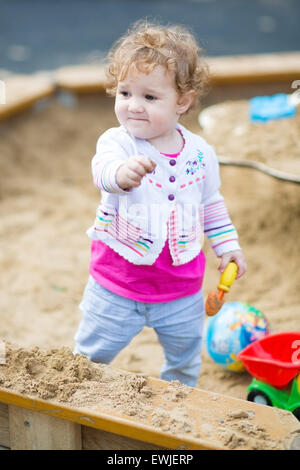 Cute little baby girl digging in sand on a playground Stock Photo