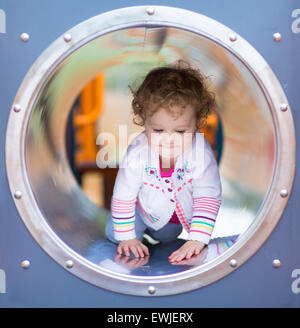 Cute curly baby girl climbing a slide on a playground Stock Photo
