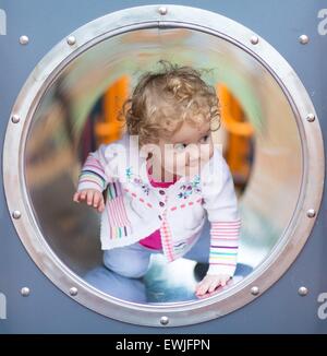 Cute curly baby girl climbing a slide on a playground Stock Photo