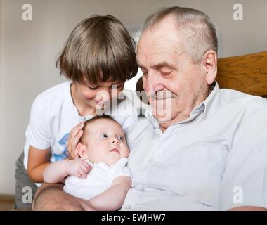 Great grandfather holding a new born baby girl next to his school age grandson Stock Photo