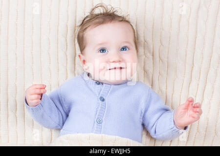 Close up portrait of an adorable baby in a warm blue knitted sweater under a cable knit blanket Stock Photo