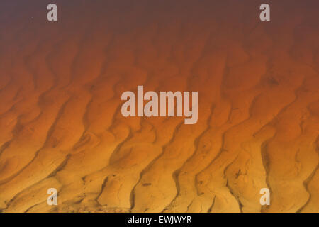 Texture wavy patterns of sand on the bottom of the peat river in red. Stock Photo