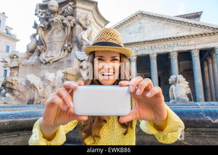 A smiling brunette tourist looks up from her mobile phone and is smiling. Behind her, Rome's Pantheon fountain and Pantheon in s Stock Photo