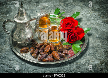 Tea, dates fruits and red rose flowers. Islamic holidays decoration. Ramadan kareem. Oriental hospitality concept. Stock Photo