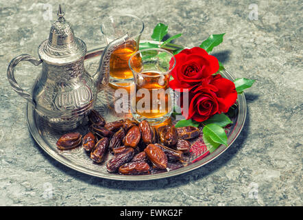 Tea, dates fruits and red rose flowers. Islamic holidays decoration. Ramadan kareem. Eid mubarak. Oriental hospitality concept. Stock Photo