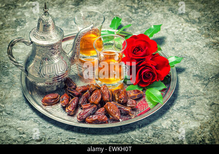 Red rose flowers with tea and dates fruits. Islamic holidays decoration. Vintage style toned picture Stock Photo