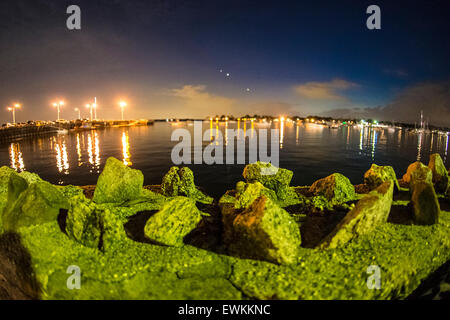 Port Washington, New York, USA. 26th June 2015. Beyond the rocks of the shoreline wall along Sunset Park, night lights shimmer on Manhasset Bay in the Gold Coast of North Shore Long Island. Credit:  Ann E Parry/Alamy Live News