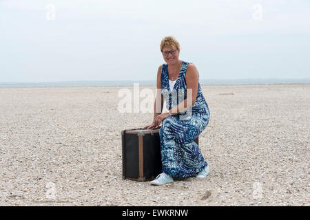 woman sitting on suitcase on the sandy beach Stock Photo