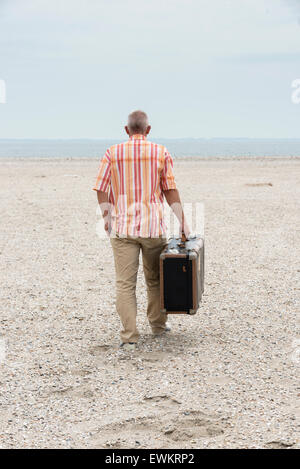 man with old vintage used suitcase walking on the beach Stock Photo