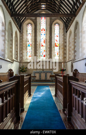 Interior of the 14th century village Church of Saint John the Evangelist showing the chancel and stained glass windows. Blue carpet leading to altar. Stock Photo