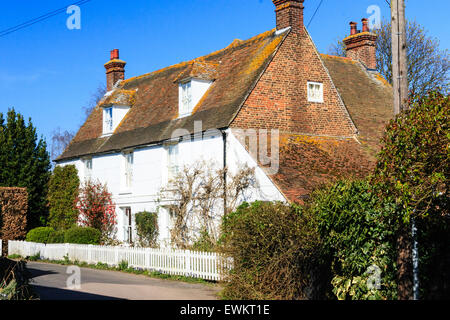 Ickham village, Kent in England. View along a large brick farmhouse painted white with small white fence around front garden with shrubs and trees in. Stock Photo