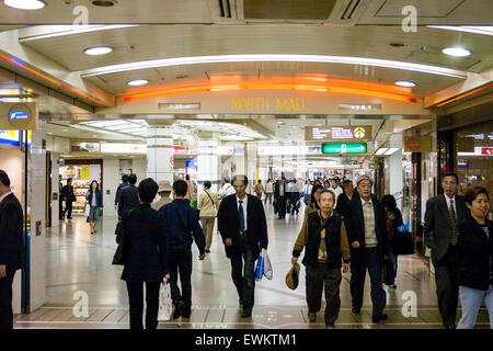 Shopping mall under the stations at Umeda in Osaka, Japan. View along a neon lit wide corridor busy with many people and with stores on either side. Stock Photo