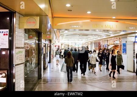 Shopping mall under the stations at Umeda in Osaka, Japan. View along a neon lit wide corridor busy with many people and with stores on either side. Stock Photo