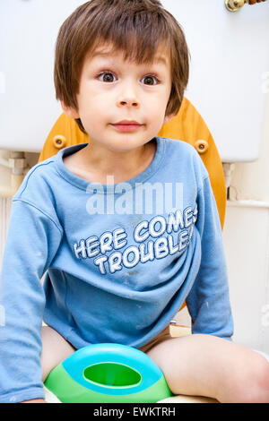 Caucasian young child, boy, 4-5 year old, facing viewer and sitting on baby seat on top of toilet during toilet training. Angelic facial expression. Stock Photo