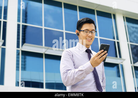 Young chinese businessman doing video conference call on smartphone and talking with bluetooth handsfree device in the street Stock Photo