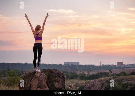 Young sporty woman with arms raised up at sunset in summer