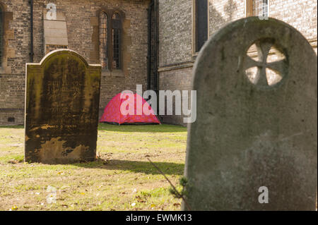 homeless no where to live so put up in red tent in churchyard charitable act helping left alone in Chelmsford city Stock Photo