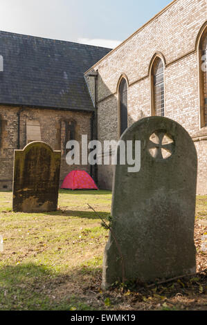 homeless no where to live so put up in red tent in churchyard charitable act helping left alone in Chelmsford city Stock Photo