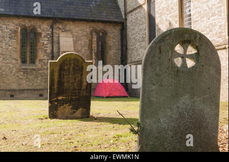 homeless no where to live so put up in red tent in churchyard charitable act helping left alone in Chelmsford city Stock Photo