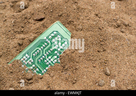 Broken Green PCB board buried in brown sand Stock Photo