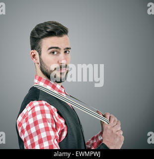 Desaturated portrait of young bearded hipster pulling his suspenders looking at camera over dark grey studio background with vig Stock Photo