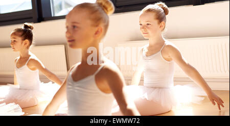 Three pretty young girls in ballet class sitting on the floor in a graceful pose in the white tutus in the warm sunshine Stock Photo