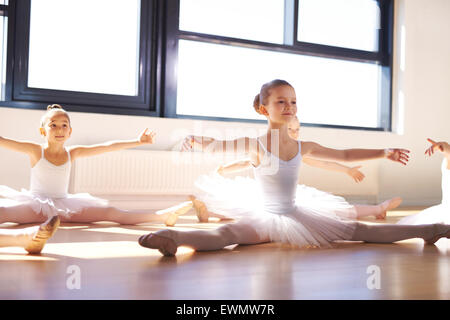 Pretty Young Ballerinas in White Tutus, Sitting on the Floor and Stretching Arms and Legs as Warm Exercise. Stock Photo
