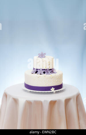 Wedding cake with violet flower decoration on table. Copy space above Stock Photo