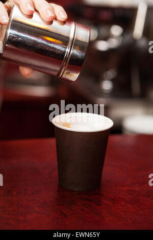 Barista, waitress making in a takeaway cup coffee with foam and cinnamon on red table. Stock Photo