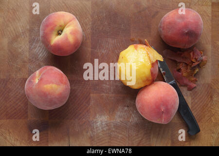 Fresh peaches on a wood cutting board, one being peeled Stock Photo