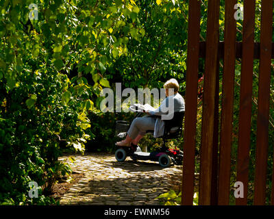 Woman in mobility scooter reading and relaxing at Trentham Gardens near Stoke on Trent Staffordshire England UK Stock Photo