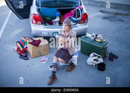 An aspiring actress applies make-up before an audition, while seated amongst her belongings near the trunk of her car. Stock Photo