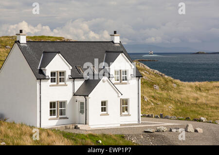 A modern house in Tarbert on the Isle of Harris, Outer Hebrides, Scotland, UK, with the ferry sailing out to sea behind. Stock Photo