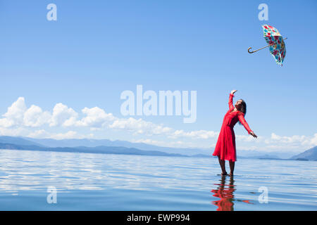 A woman in red standing on water with an umbrella floating above her. Stock Photo