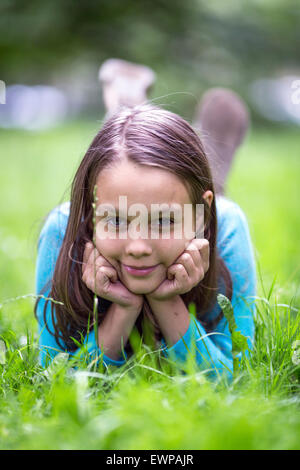 Portrait of cute little girl lying in green grass. Stock Photo