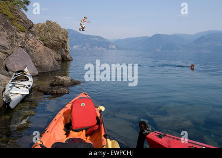 Boy jumping off cliff into lake Stock Photo