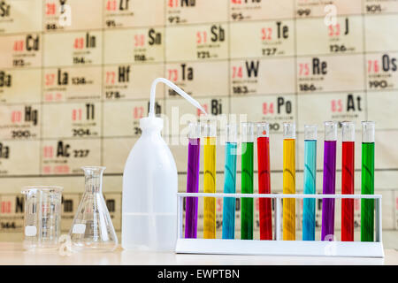 Chemistry with colored test tubes and glass in front of wallchart showing periodic table Stock Photo