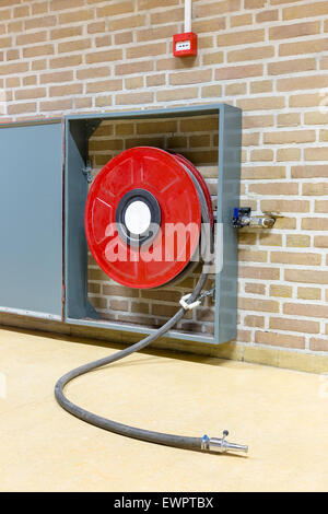 Red fire hose on reel hanging at wall in school building Stock Photo
